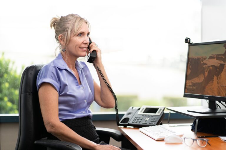 Woman on the phone offering support in the CADA office. Woman is wearing a purple top, has blonde hair and light skin.