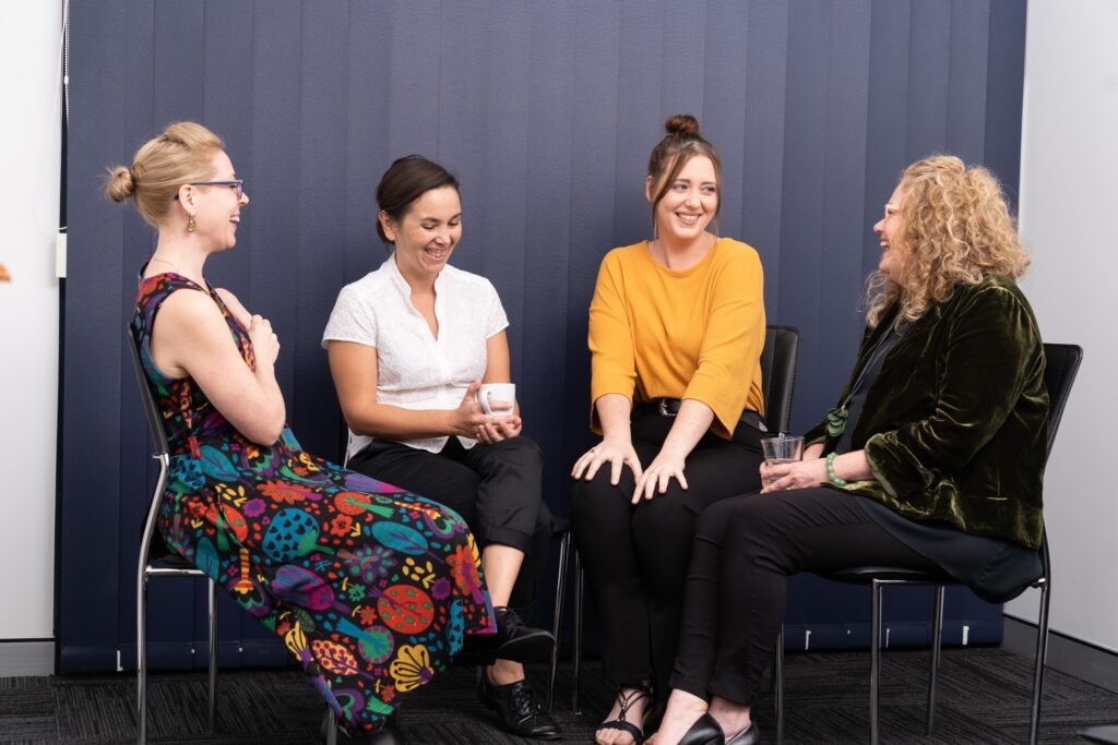 Four women sitting in a semi-circle, laughing and supporting each other.
