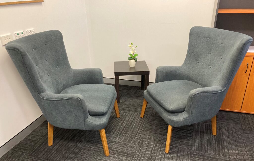 Counselling room with two blue arm chairs facing towards each other.
